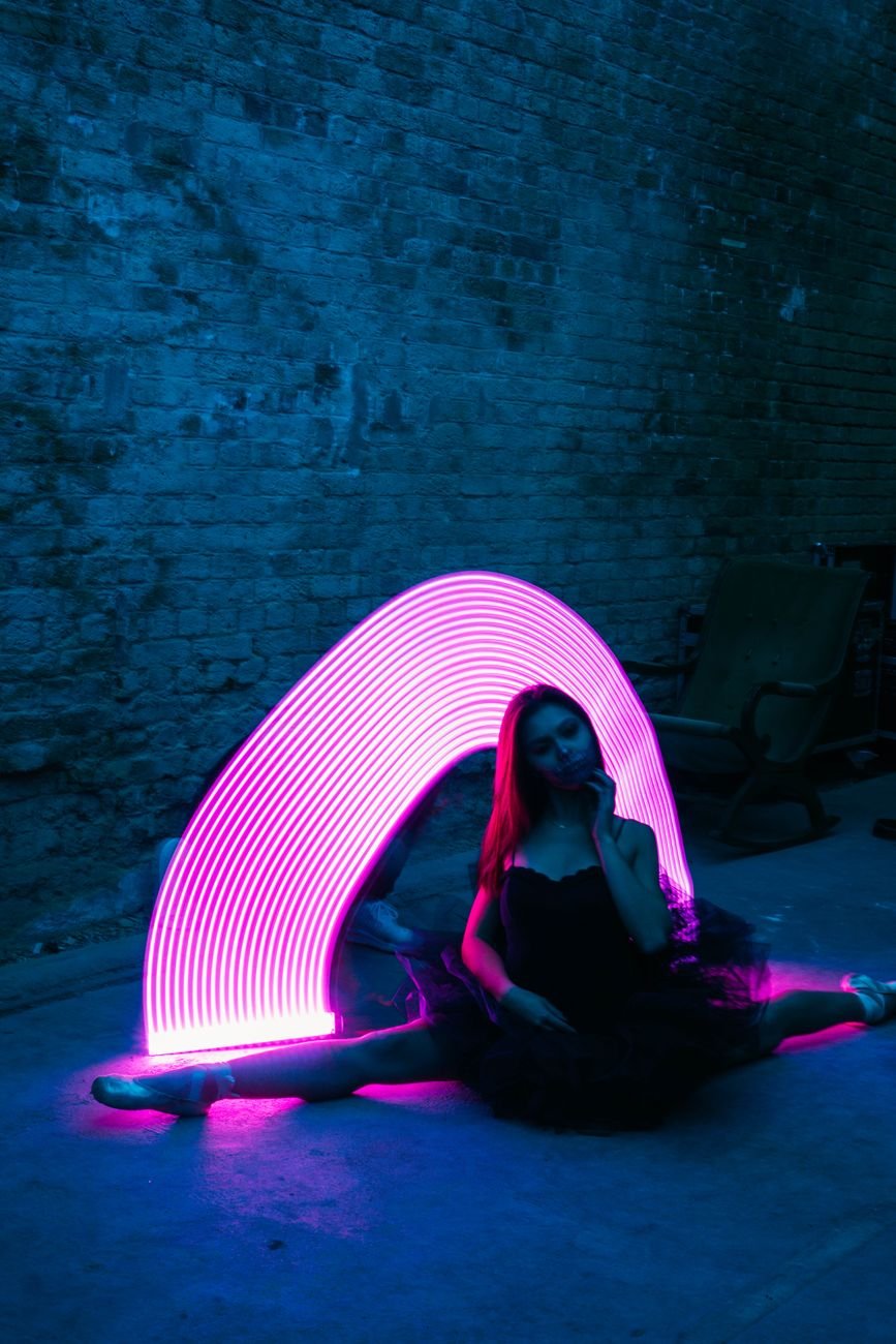 Artistic portrait of a woman in a leg split with neon light trails in a dark studio